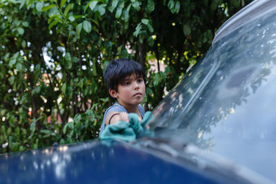 Girl with short black haircut washing blue car in the garden