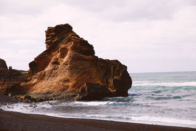 Rock formation at sea shore against sky