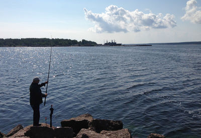 Man fishing in sea against sky