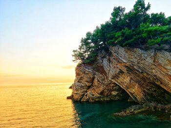 Rock formation in sea against sky during sunset