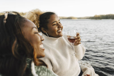 Smiling woman enjoying wine with female friend at lakeshore