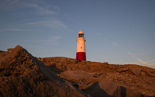 Lighthouse on rock by building against sky