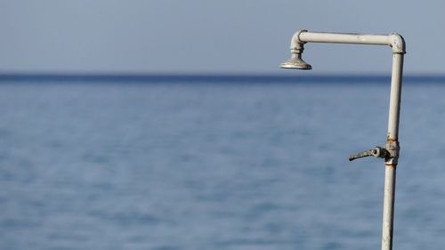 Close-up of metal railing against sea against clear sky