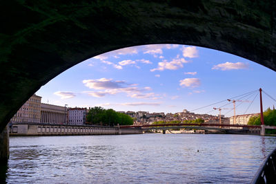 Arch bridge over river in city against sky