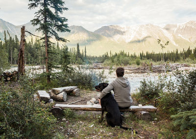 Rear view of man with dog sitting by river