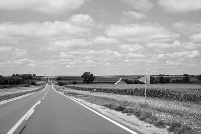 Empty road amidst field against sky