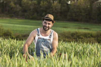 Portrait of farmer wearing hat while sitting on agricultural field during sunset