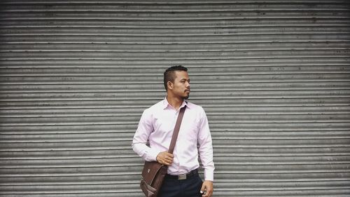 Businessman looking away while standing against closed shutter