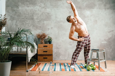 Full length of shirtless man standing on table at home