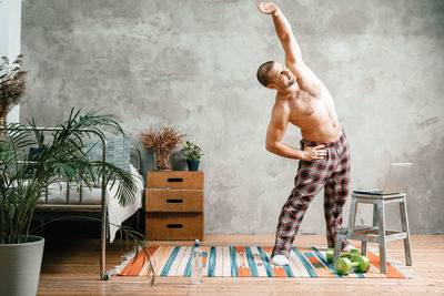 The athlete in home pajamas does morning exercises, bends and pulls his hand 