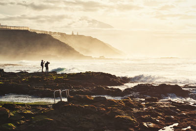 People standing on rock by sea against sky