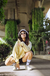 Fashionable woman wearing sunglasses squatting on footpath