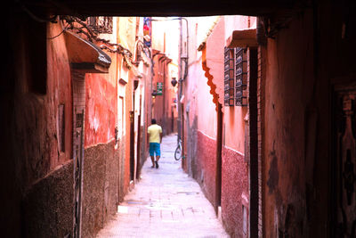 Rear view of man walking on narrow street amidst buildings