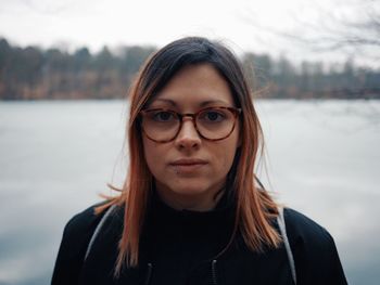 Close-up portrait of young woman wearing eyeglasses against lake