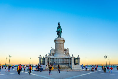 Statue in square at sunset with people