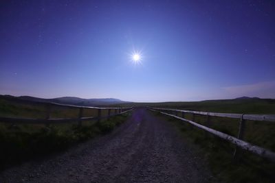 Road amidst field against clear sky at night