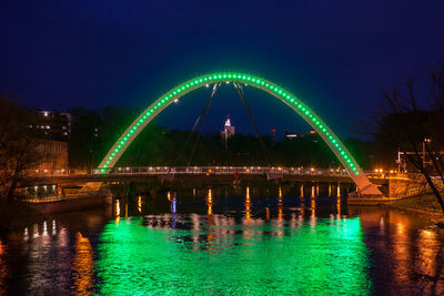 Illuminated ferris wheel by river against sky at night