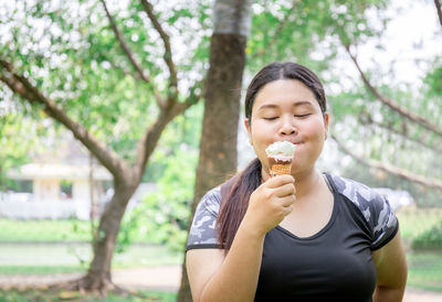 Portrait of mid adult woman holding ice cream against trees