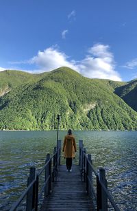 Rear view of woman standing on pier over lake against mountains