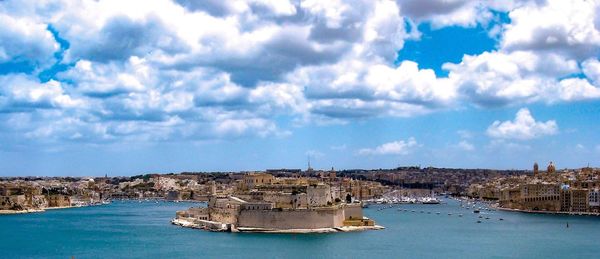 Panoramic view of buildings by sea against cloudy sky