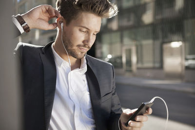 Young businessman listening music through mobile phone outdoors