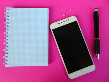 Directly above view of pen and blank diary with mobile phone on pink background