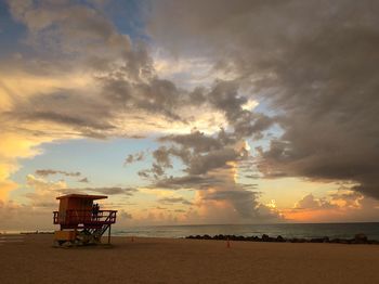 Lifeguard hut at beach against cloudy sky during sunset