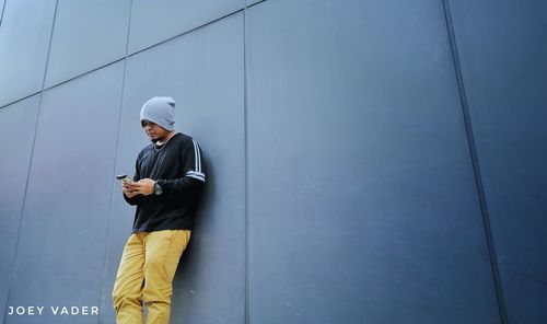 Man using mobile phone while standing on wall