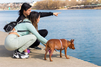 Young girl and her mother on relaxing vacation by the lake with their cute miniature pinscher.