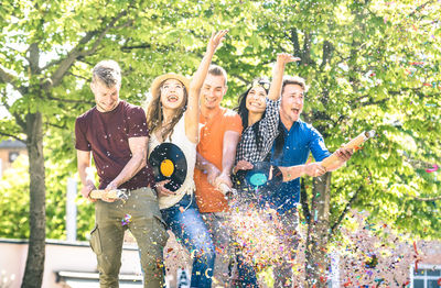 Cheerful friends with confetti while standing against trees