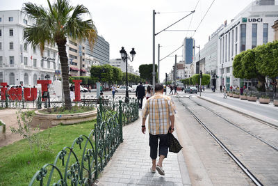 Rear view of people walking on footpath in city