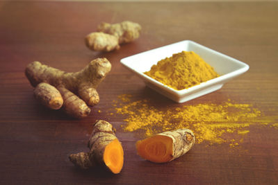 Close-up of tumeric root and powder on wooden table