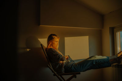 Side view of young woman sitting on chair at home