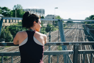 Rear view of exhausted sportswoman leaning on railing at bridge