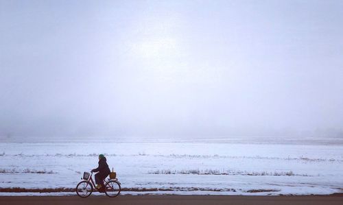 Woman riding bicycle against sky during winter