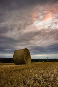 Hay bales in field against cloudy sky