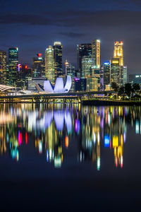 Illuminated buildings by river against sky at night