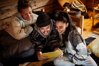 High angle view of smiling friends watching movie over digital tablet while relaxing in cottage