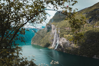 Scenic view of fjord and waterfall amidst trees against mountains