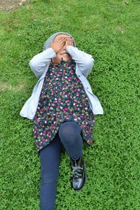High angle view of girl with hands covering eyes lying on grassy field in park