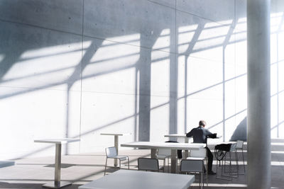 Rear view of businessman sitting at table against concrete wall