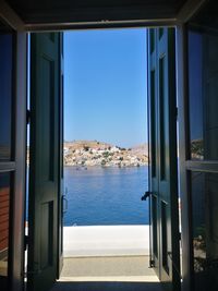 Buildings by sea against clear sky seen through glass window