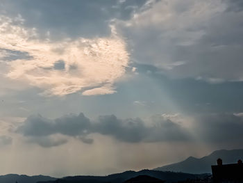 Low angle view of sunlight streaming through clouds