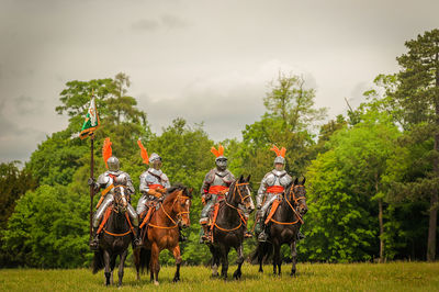 Men riding horses on field against sky