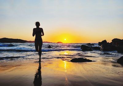 Rear view of man standing at beach against sky during sunset