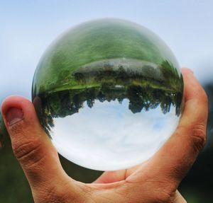 Close-up of human hand holding crystal ball against trees