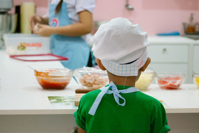 Rear view of boy in chef hat cooking food in kitchen