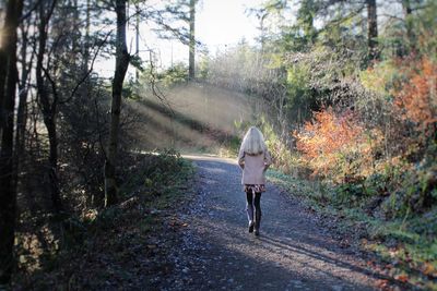 Rear view of woman walking on road in forest