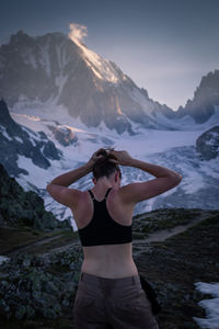 Rear view of woman tying hair while standing against mountain during winter