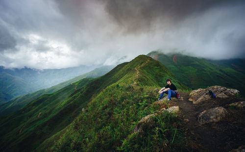 Woman sitting on scenic mountain range against sky